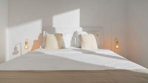 Un lit bien fait, avec du linge de lit blanc et deux oreillers, deux appliques murales et une décoration simple et épurée.