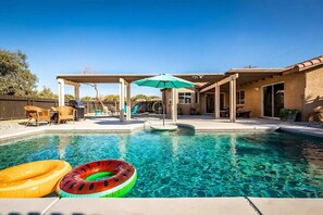 Quintal com piscina, móveis de exterior e uma pérgula com guarda-sol.