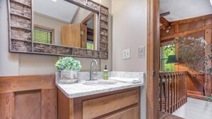 A bathroom with a wooden vanity, a marble sink, a mirror, and a plant. - Rushing Creek Retreat, Serene Cabin with Great Views! (Sylva)