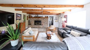 A living room with a stone fireplace, wooden ceiling beams, a television, and a sofa. - Loveta Hideaway (Mount Shasta)