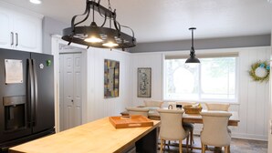 A kitchen with a wooden island, white cabinetry, a black refrigerator, and a dining area with chairs and a table. - Loveta Hideaway (Mount Shasta)
