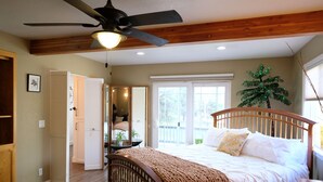 A bedroom with a wooden bed, a ceiling fan, and a large window. - Loveta Hideaway (Mount Shasta)