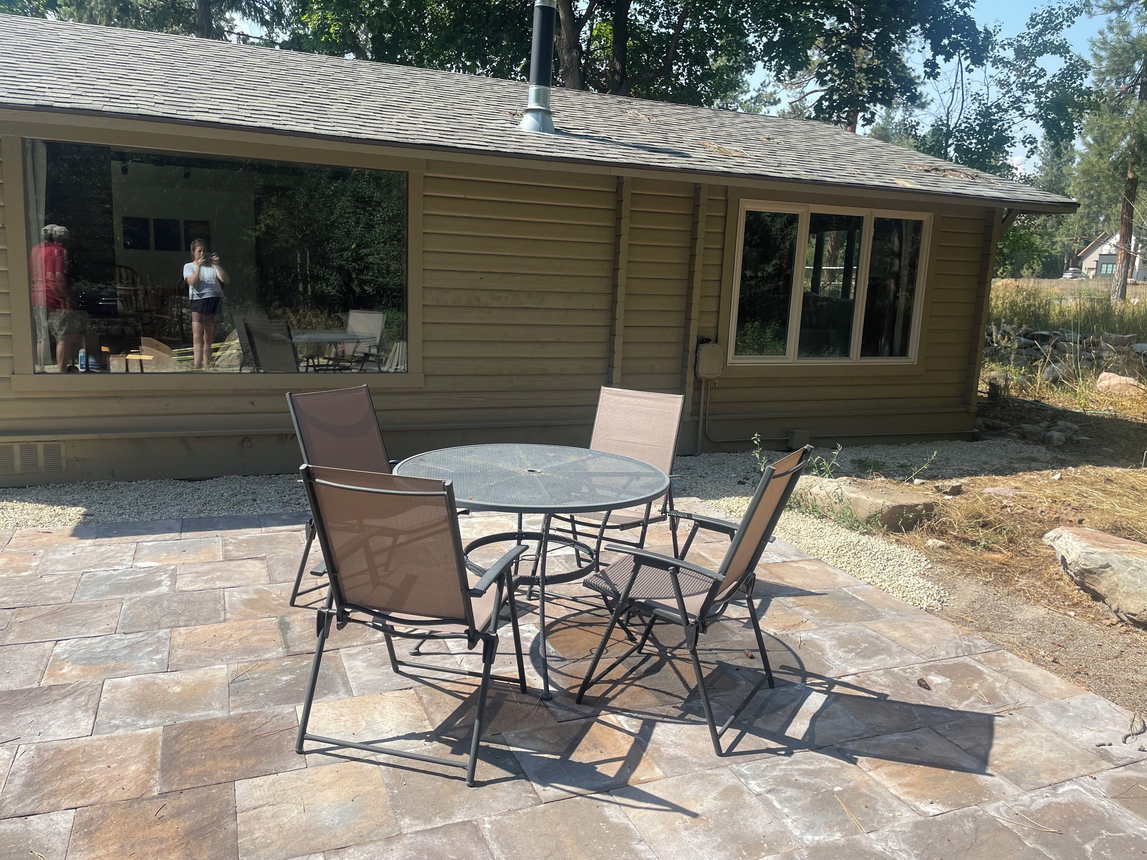 A patio with a round table and four chairs, a covered outdoor seating area, and a house with a tiled roof and large windows.
