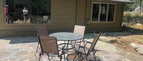 A patio with a round table and four chairs, a covered outdoor seating area, and a house with a tiled roof and large windows.
