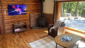 A cozy living room with a wooden wall, a television, a fireplace, and a view of the outdoors. - Cozy Rattlesnake Creekside Cabin Retreat  (Missoula)