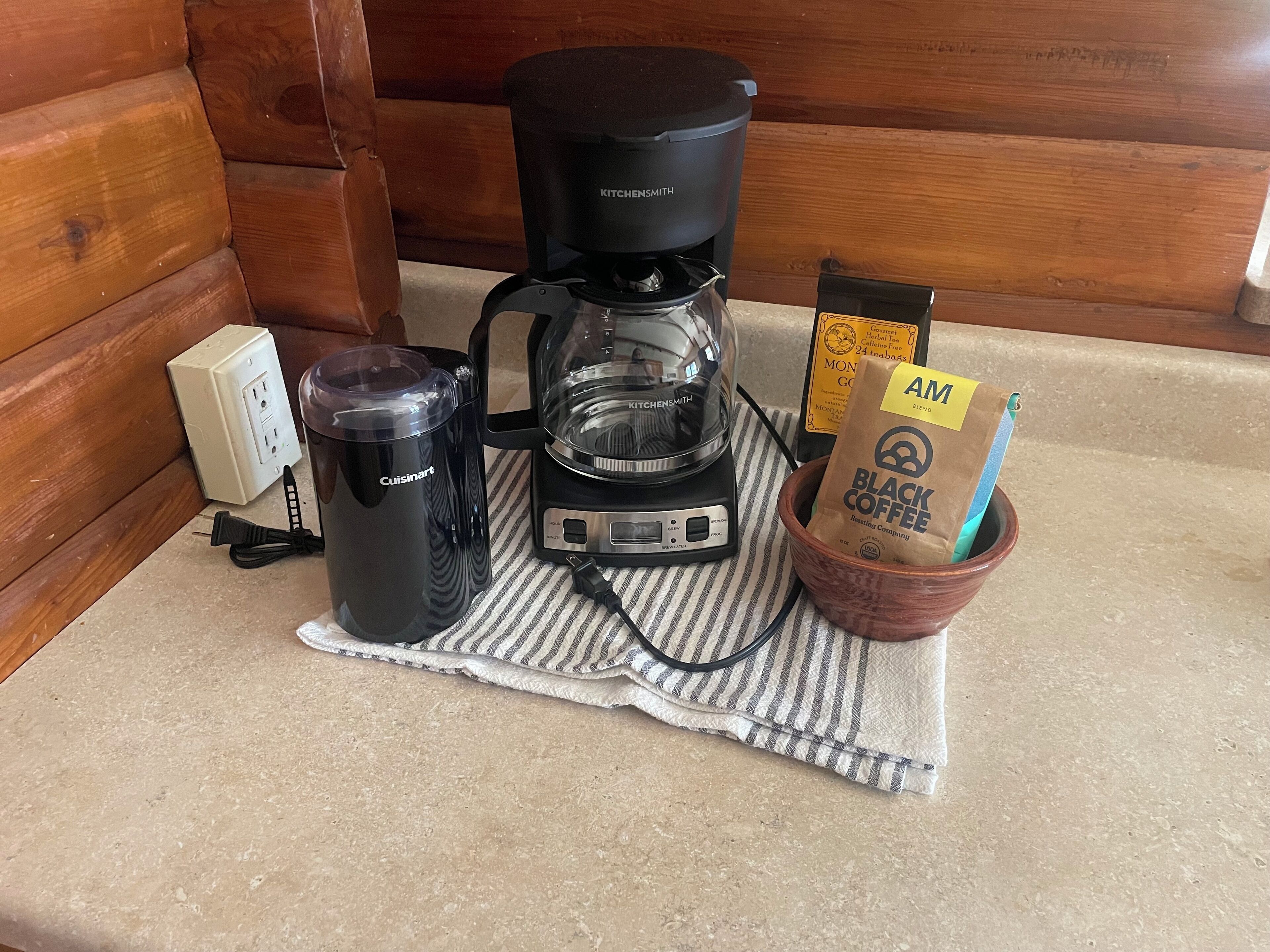A kitchenette with a coffee maker, a water bottle, a coffee bag, and a coffee mug on a countertop.