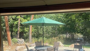 A patio with a stone table and chairs, a green umbrella, and a barbecue grill. - Cozy Rattlesnake Creekside Cabin Retreat  (Missoula)