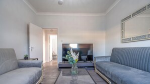 Un salon moderne avec deux canapés gris, un téléviseur à écran plat et un vase de fleurs posé sur une table basse carrelée.