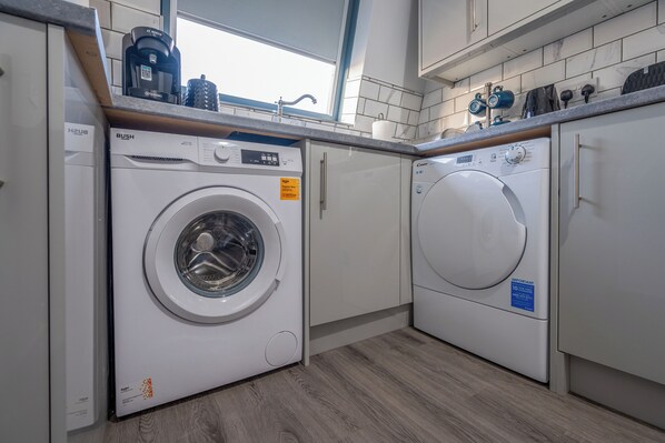 A modern laundry room with two front-loading washing machines, a coffee machine, and a window providing natural light.