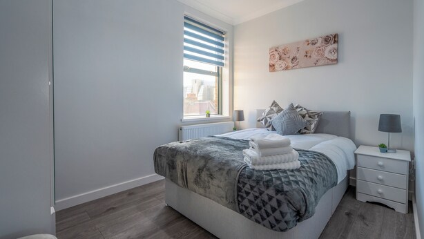 Une chambre moderne avec un grand lit, une table de chevet, une commode, une fenêtre avec des stores et une œuvre d’art accrochée au mur.