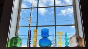 Une fenêtre à carreaux et divers vases en verre exposés.