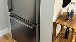 Un réfrigérateur en acier inoxydable doté d’un appareil à glaçons intégré, placé à côté d’une table d’appoint en bois sur laquelle se trouve un objet noir.