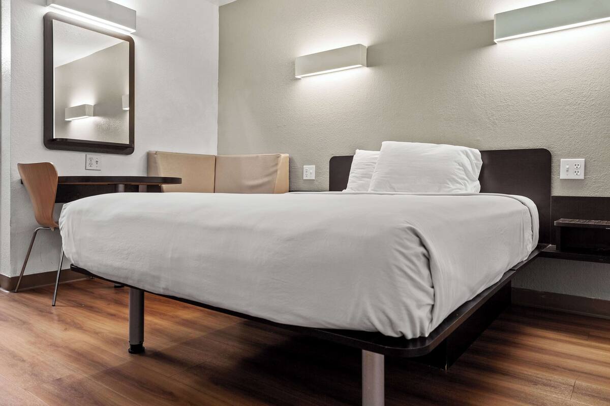 Ein modernes Hotelzimmer mit einem großen Bett, einem Schreibtisch, einem Stuhl und einem Spiegel.
