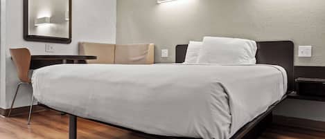 A modern hotel room with a large bed, a desk, a chair, and a mirror.