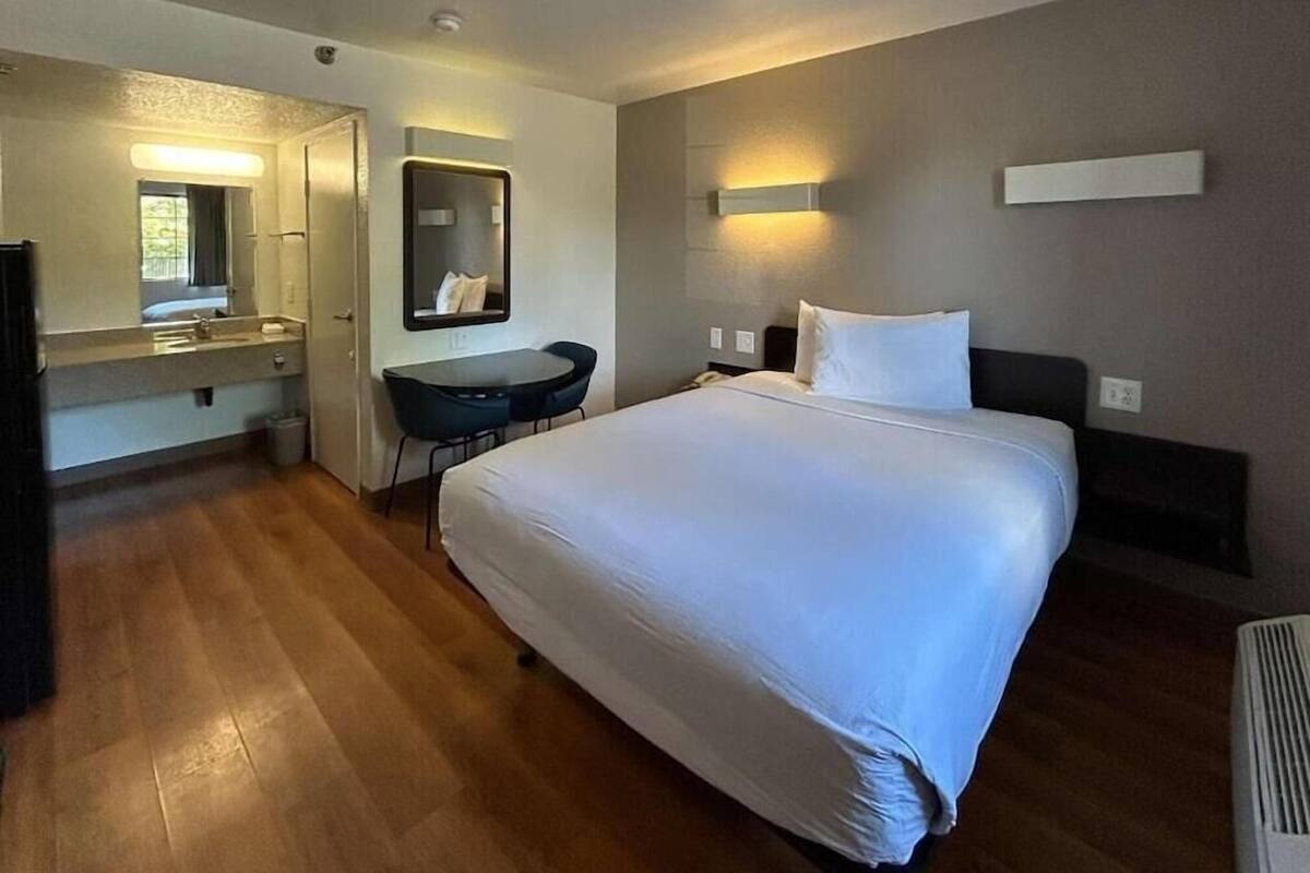 Ein Hotelzimmer mit einem großen Bett, einem Schreibtisch, einem Sessel, einem Spiegel und einem kleinen Tisch.