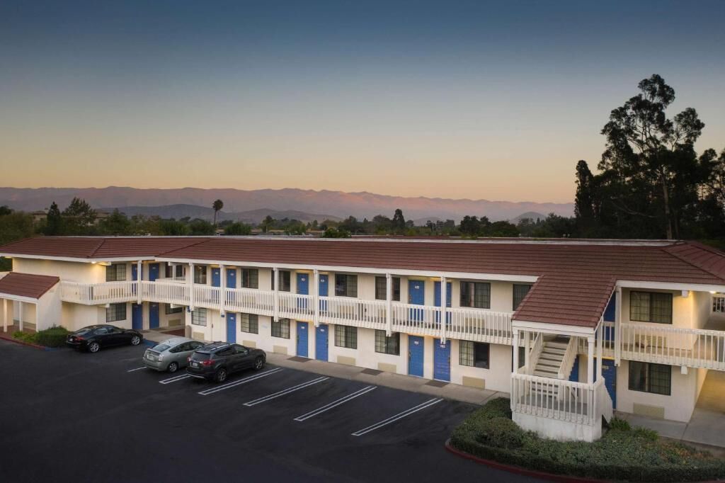 A motel with a two-story structure, a parking lot, and a view of distant mountains.