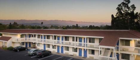 A motel with a two-story structure, a parking lot, and a view of distant mountains.