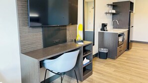 A modern hotel room with a flat-screen TV, a desk with a chair, a coffee machine, and a trash bin. - Studio 6 Hornepayne, ON (Hornepayne)
