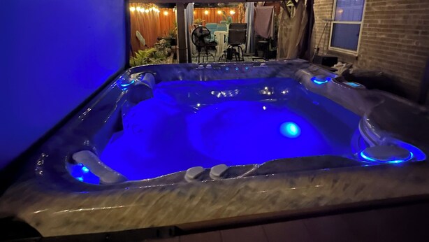 Ett bubbelbad med blått ljus, omgivet av ett takförsett område med ljusslingor.