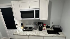Ett kompakt kök med vita skåp, en mikrovågsugn, en kaffebryggare och ett handfat.