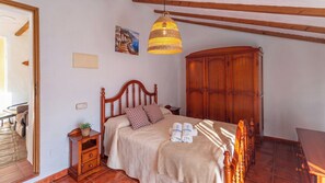 A bedroom with a wooden bed, a nightstand, a wicker lamp, a wardrobe, and a painting on the wall.