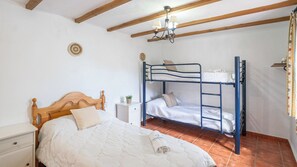 Un dormitorio con una cama de madera, una litera, una mesita de noche y una pequeña mesa con una planta.