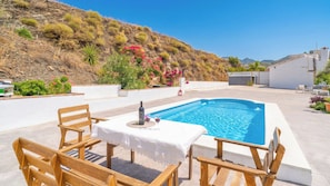 A pool area with a table and chairs, surrounded by a white building and a hillside. - Reiner Canillas de Albaida by Ruralidays (Málaga)