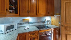 A kitchen with wooden cabinets, a white microwave, a stove, and a sink. - Reiner Canillas de Albaida by Ruralidays (Málaga)