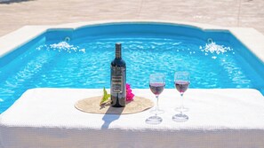 A bottle of wine and two glasses on a table by a pool.