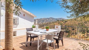 Eine Terrasse mit Tisch und Stühlen, einem Blumentopf und Blick auf eine hügelige Landschaft.