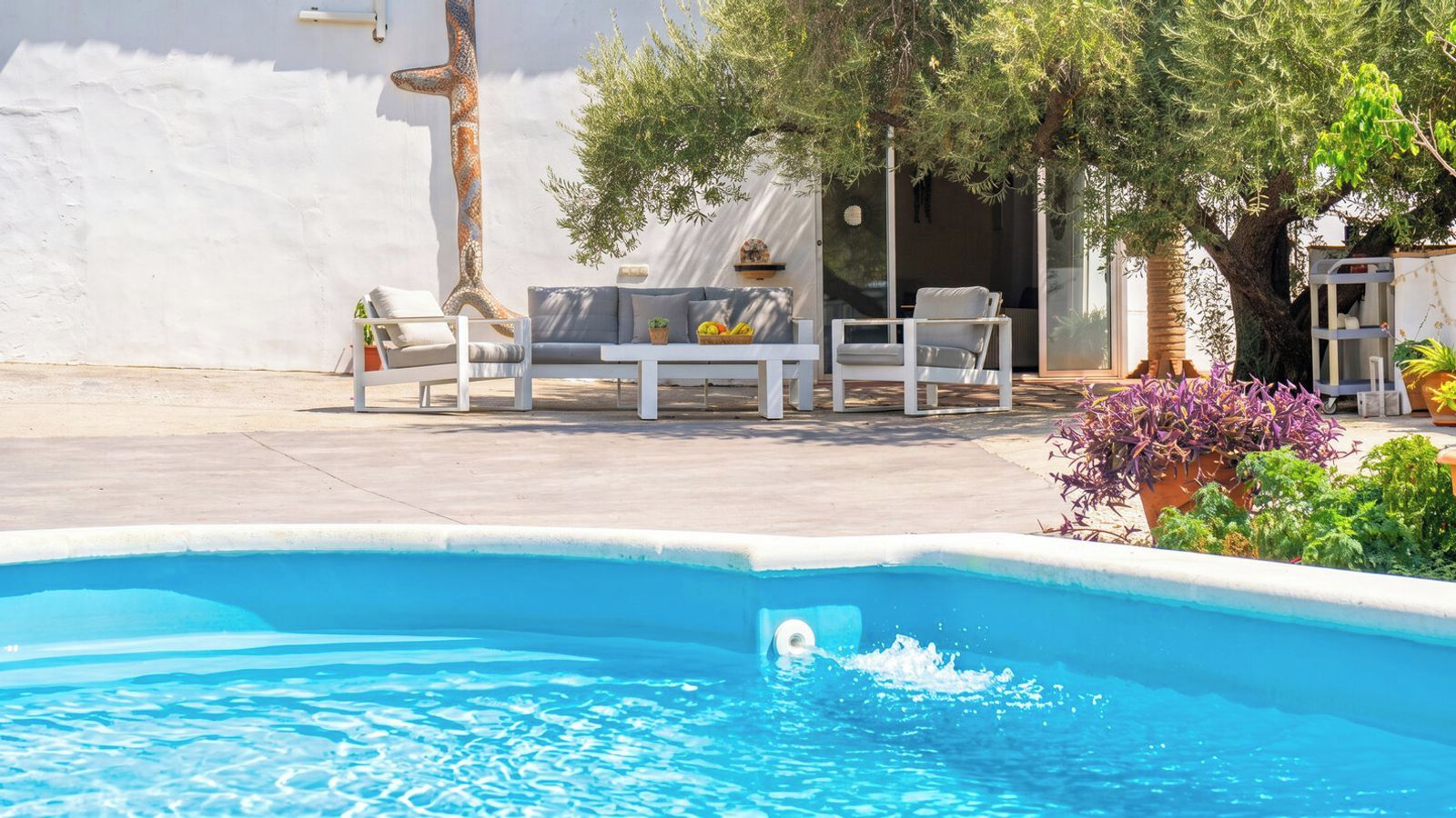A swimming pool with a white deck, lounge chairs, and potted plants.