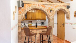 A kitchen with a stone archway, wooden cabinets, a microwave, and two bar stools.