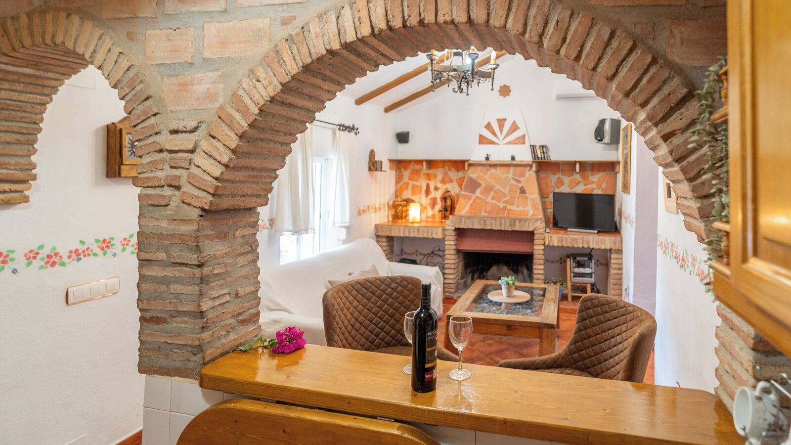 A dining area with a brick archway, a fireplace, and a television in the background.
