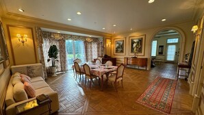 A dining area with a table set for four, surrounded by wooden chairs. There is a sofa with cushions and a small table with a lamp. The room has wooden flooring and a patterned rug. - Chateau Herbe - Shakespeare 1 Bedroom Suite w/ Kitchen (Ashland)