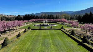 A well-manicured garden with a central circular lawn, surrounded by neatly trimmed hedges and flowering trees. - Chateau Herbe - Shakespeare 1 Bedroom Suite w/ Kitchen (Ashland)