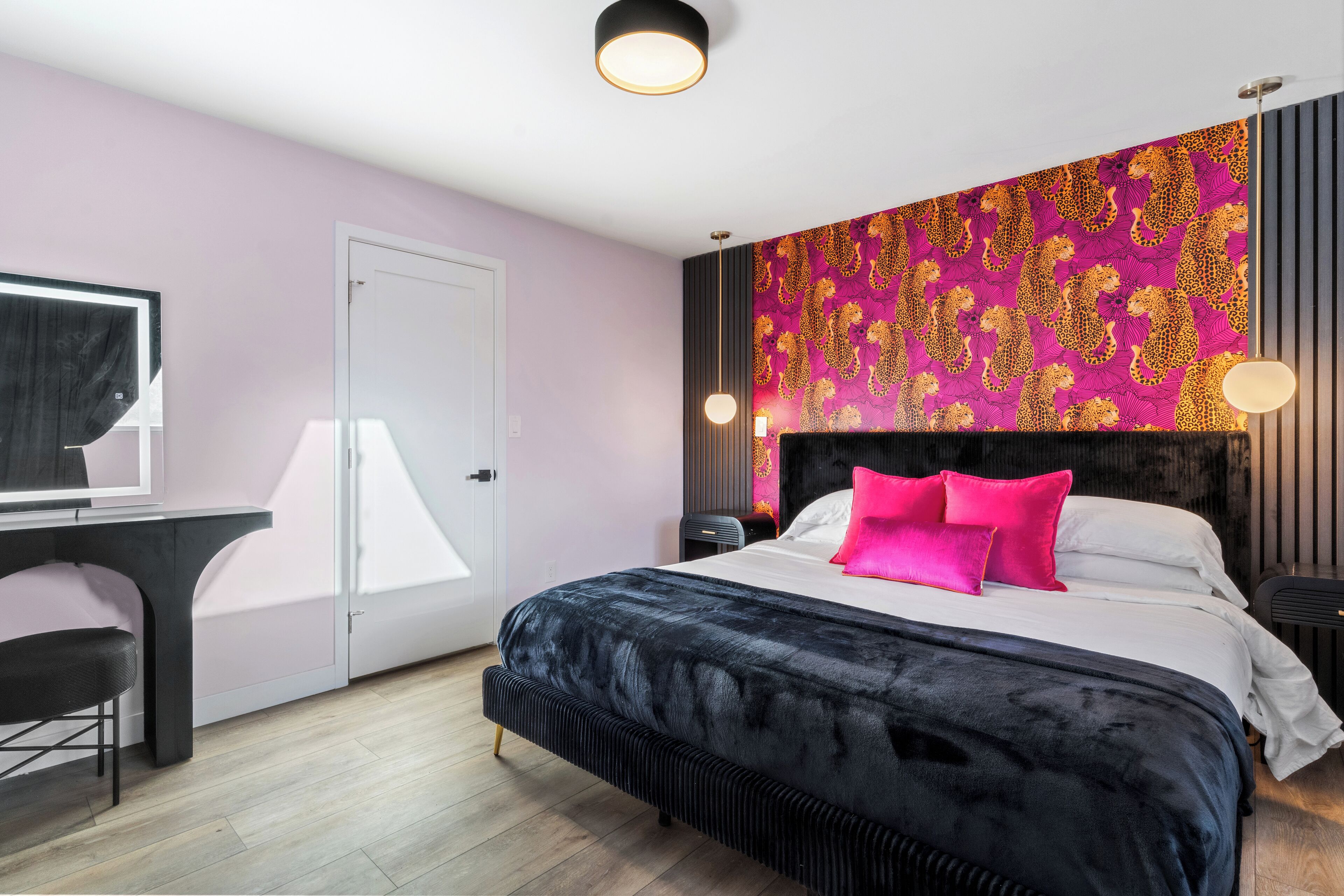 A modern bedroom with a large bed, a desk, and a vibrant patterned wall.