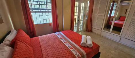 A bedroom with a bed, a ceiling fan, a window with curtains, and a sliding door closet.