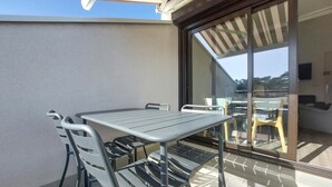 A patio with a metal table and chairs, a sliding glass door, and a view of the surrounding area.