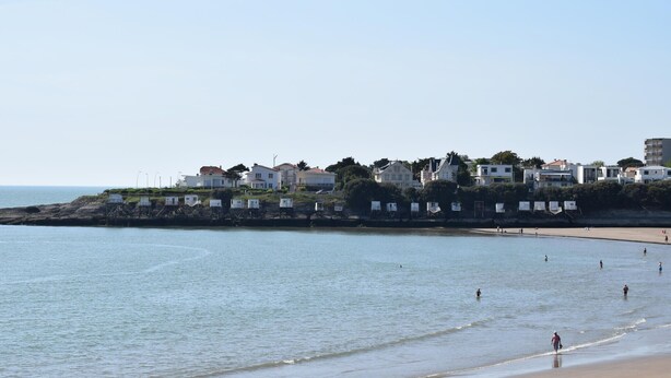 A coastal town with a beach, houses, and a rocky shoreline.