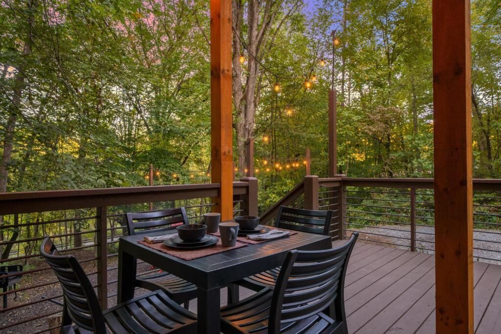 A wooden deck with a table set for dining, surrounded by chairs, overlooking a forested area.
