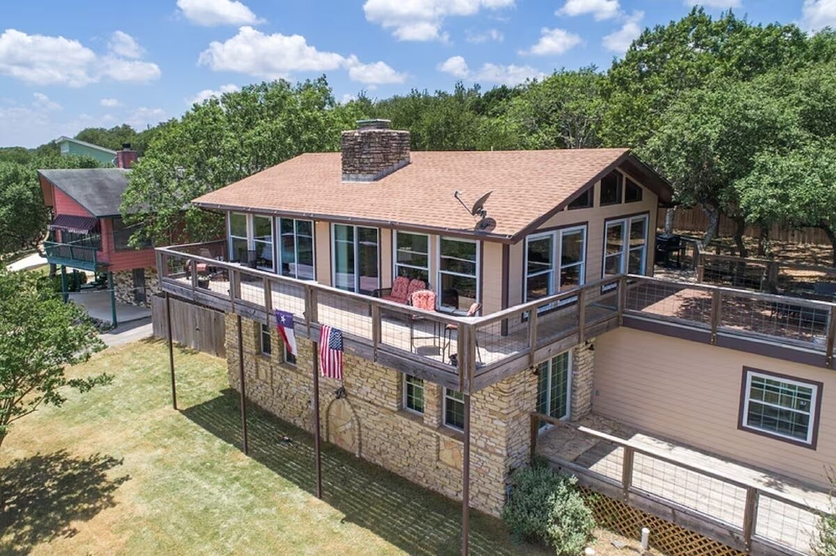 A two-story house with a balcony, stone exterior, and a fenced backyard.