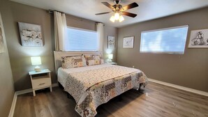 Un dormitorio con cama, mesitas de noche, ventilador de techo y obras de arte en las paredes.