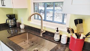 A kitchen with a stainless steel sink, a coffee maker, and a red utensil holder. - 2nd-Story Covered Deck with Lake View - 2 Kings, 3 Queens! (Canyon Lake)
