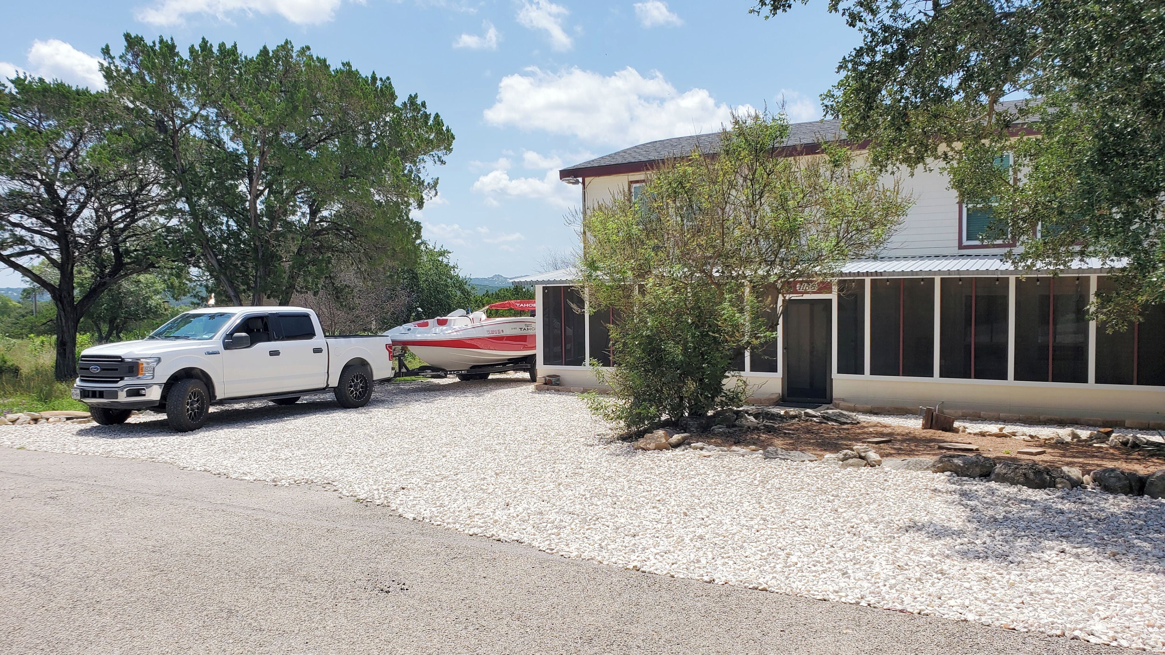 A white pickup truck parked in front of a house with a boat trailer attached.