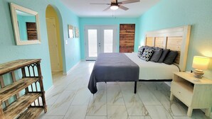 A bedroom with a bed, bedside table, lamp, wooden bench, and a ceiling fan. - 2nd-Story Covered Deck with Lake View - 2 Kings, 3 Queens! (Canyon Lake)