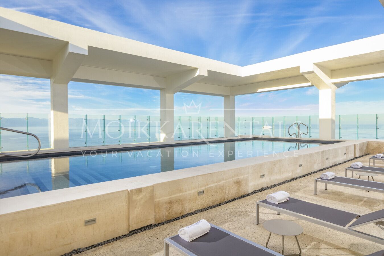 A rooftop infinity pool with lounge chairs and a glass railing, offering a view of the ocean.