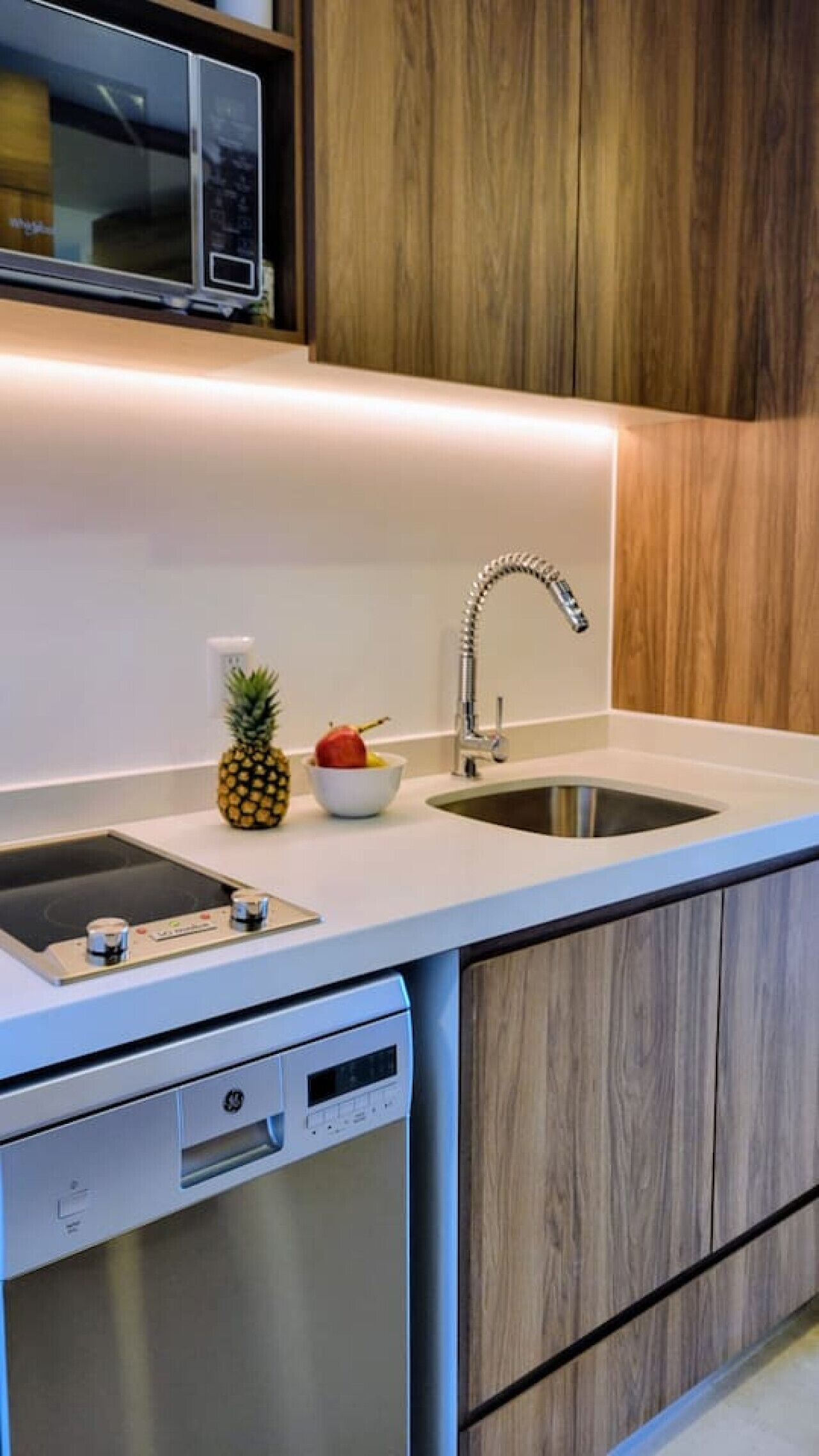 Une cuisine moderne avec un plan de travail blanc, un évier en acier inoxydable et des armoires en bois.