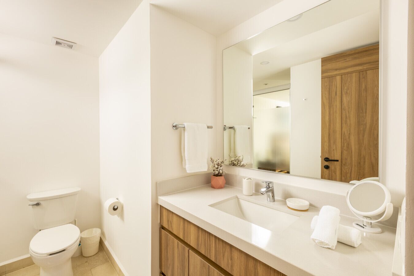Un baño moderno con inodoro, lavamanos, espejo y mueble de madera.