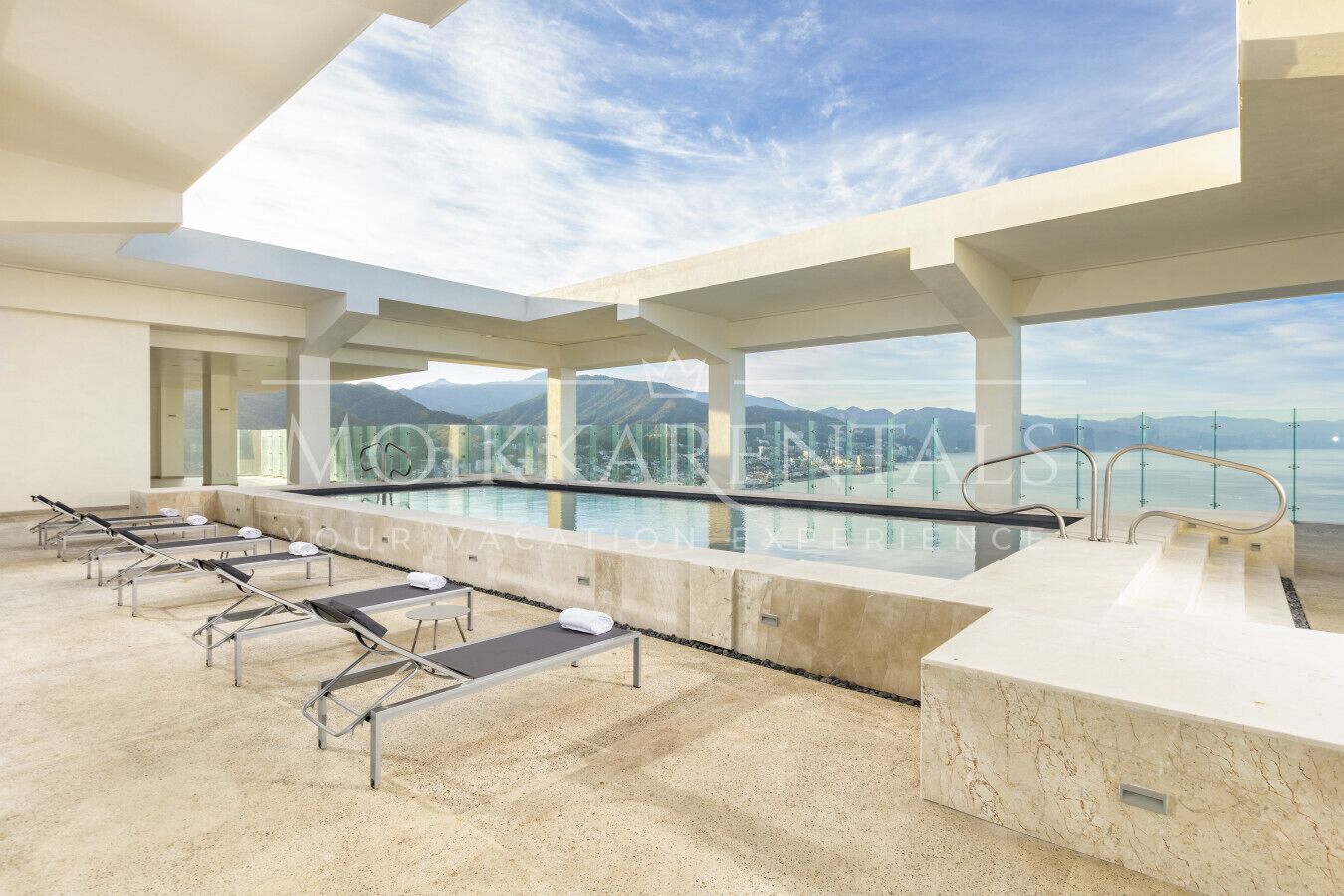 A modern indoor pool area with lounge chairs and a view of mountains and water.