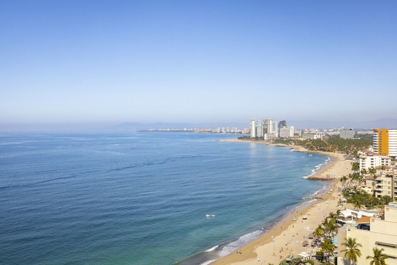 Un paysage urbain côtier avec une plage, des immeubles de grande hauteur et un ciel dégagé.